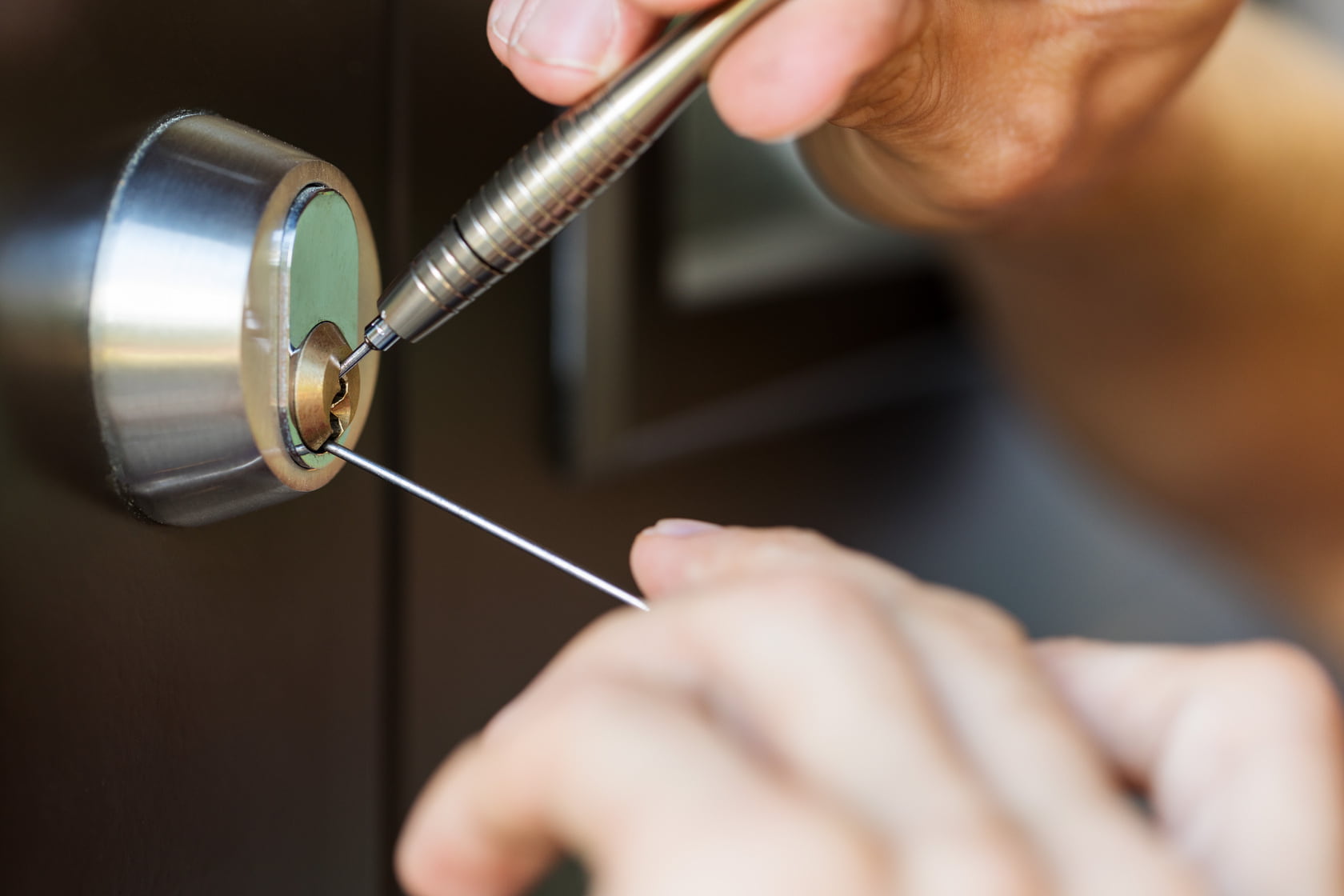 closeup of locksmith hands using pick tools to open locked door