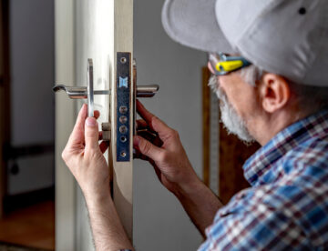 Door lock installation, repair, or replacement service. Door hardware installer locksmith working with open white door indoor