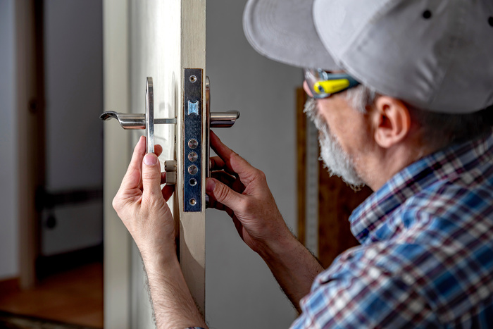 Door lock installation, repair, or replacement service. Door hardware installer locksmith working with open white door indoor