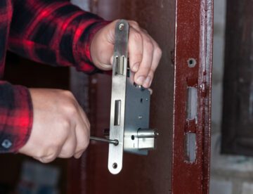 A male locksmith installs a new door lock on a metal door